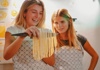  Two women holding a knife and pasta and smiling 