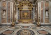 A grand, symmetrical hallway in a historic church, adorned with golden details, marble columns, and religious artwork.