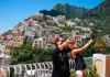 A group of tourists taking selfies in front of the colorful cliffs in Positano, Italy. 