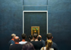 A woman in the Louvre taking a photo of the Mona Lisa while listening to their guide from The Tour Guy.