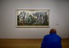 A visitor in a blue coat sits on a bench, admiring a large Picasso painting displayed on a white gallery wall.