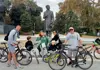 Family-friendly bike tour group stopping at a statue inside Seville’s María Luisa Park.