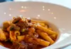 Bowl of pasta topped with Neapolitan ragù sauce in a white dish.