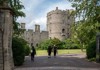 Visitors walk toward the entrance of Windsor Castle, passing by stone towers surrounded by lush greenery.