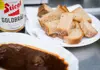 Plate of sliced rustic bread served with dark Austrian beef goulash and a bottle of Stiegl Goldbräu beer.