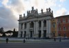 The grand façade of the Basilica of St. John Lateran, with towering statues and intricate columns against a cloudy sky.