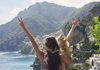 An image of  tourists looking at Positano with their arms stretched out. 