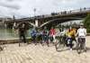 Guided bike tour group posing beside Seville’s Triana Bridge during a stop along the river.