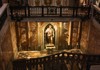 A dimly lit chapel features a statue of the Virgin Mary, framed by dark wooden railings and golden accents.