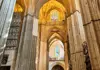 Interior of Seville Cathedral featuring tall Gothic arches and stained-glass windows illuminated by natural light.