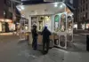 Two people ordering food at an outdoor street kiosk at night.