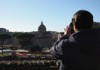 An image of a woman taking a photo of the Rome skyline.