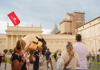 Two tourists having their picture taken in front of the School of Athens. 