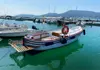 Small wooden excursion boat moored in a marina with hills and other boats in the distance.