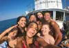 Passengers taking a group selfie on the bow of a boat during a seaside excursion.
