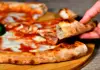 Close-up of a slice of Neapolitan pizza crust being lifted from a wooden serving board.