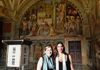 Two tourists having their picture taken in front of the School of Athens. 
