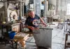 Murano glassmaker working at his bench with tools, furnace, and equipment around him