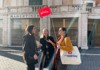 A tour guide holds a red sign while leading a small group outside a historic site, engaging in conversation.