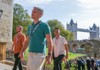 A group of tourists walking into the Tower of London with Tower Bridge in the background.
