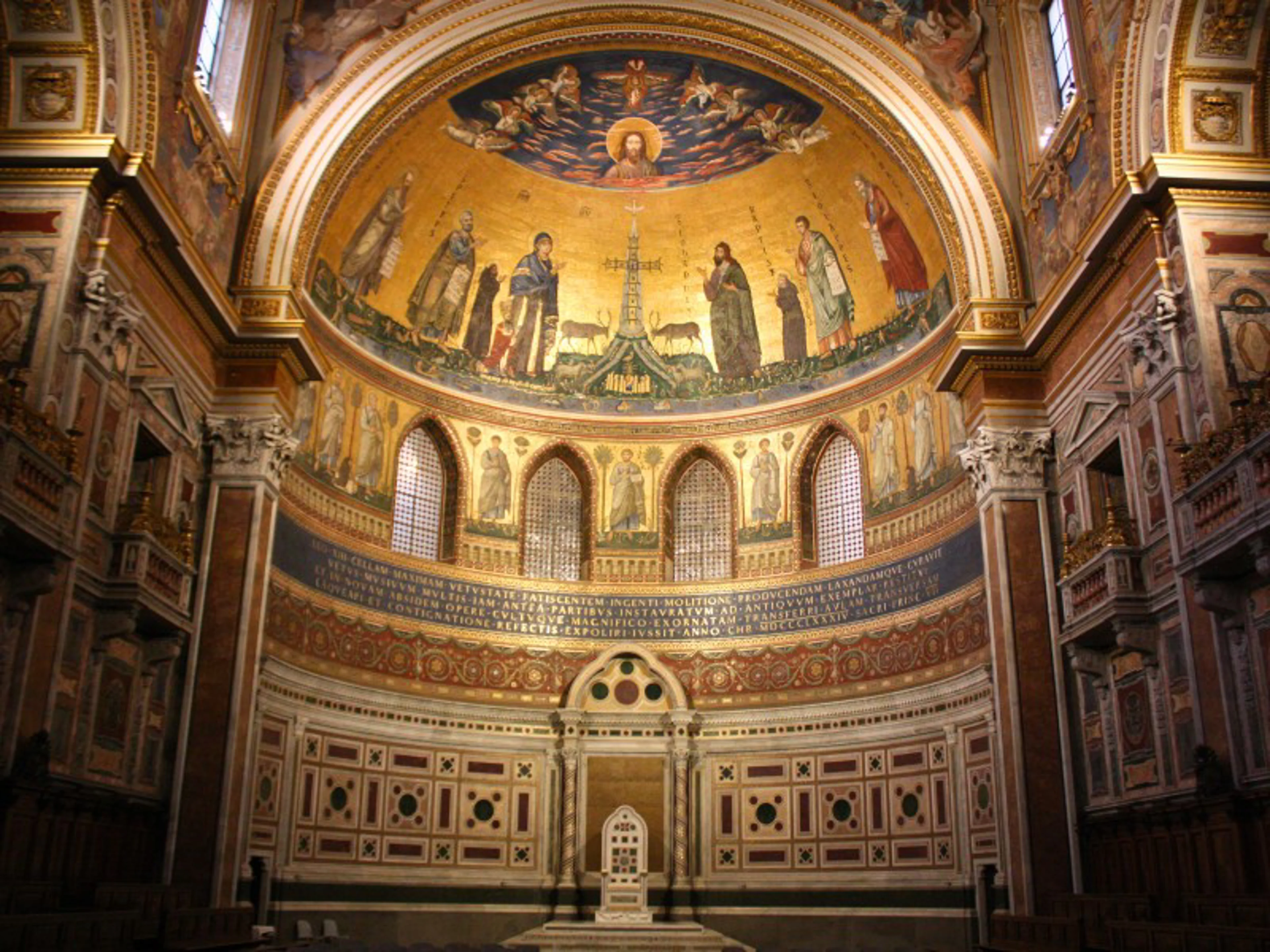 A golden mosaic of Christ and saints adorns the apse of a historic church, illuminated by warm lighting.