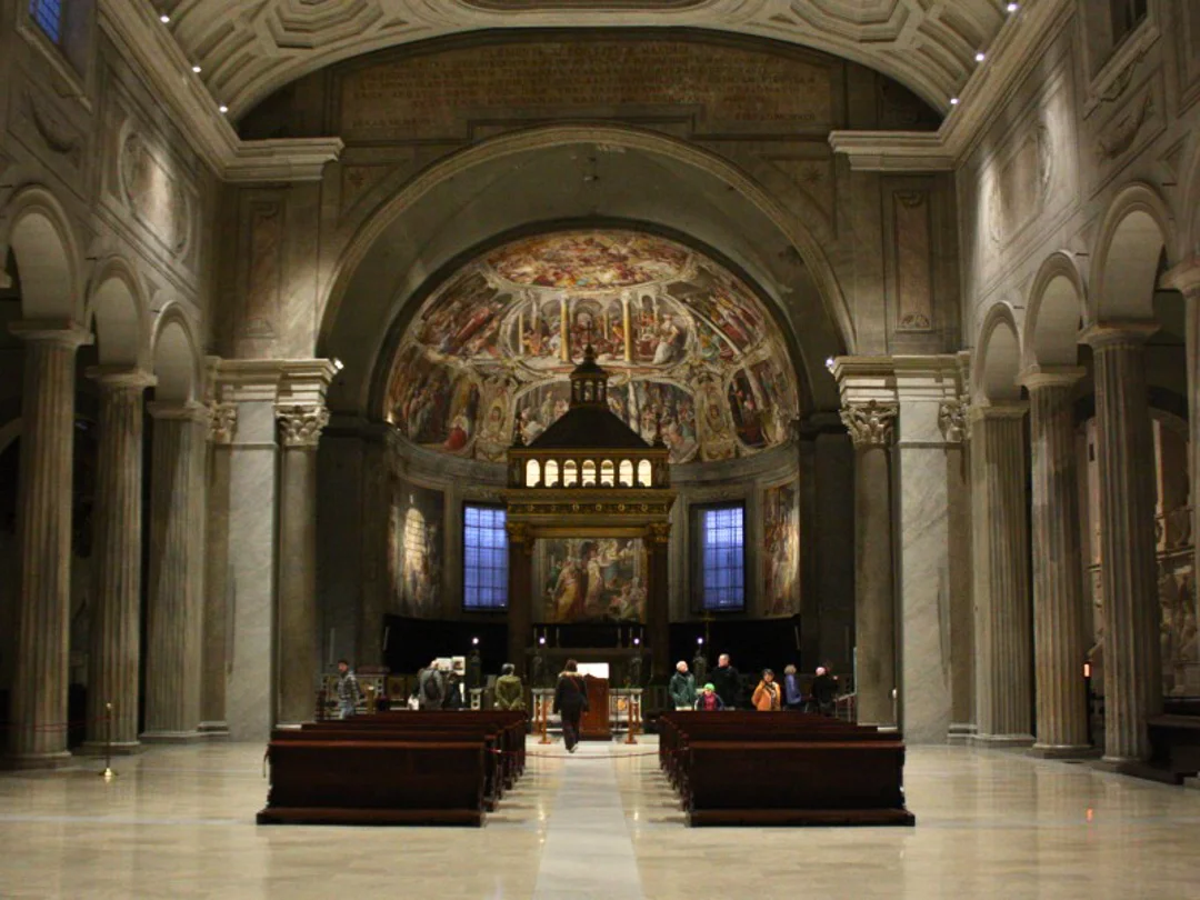 A dimly lit church interior features an ornate altar, framed by towering columns and intricate mosaics.