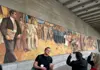 Tour guide speaking in front of a large socialist-era mural in Berlin as visitors take photos