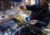 Vendor squeezing fresh lemon over steamed mussels at a street food stall