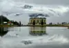 Mountain hotel reflected in a lake with misty peaks rising behind it