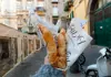 Hand holding two pieces of fried pizza dough wrapped in branded paper on a Naples street.