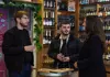 Food tour group sampling drinks inside a specialty beer shop lined with bottles on wooden shelves.