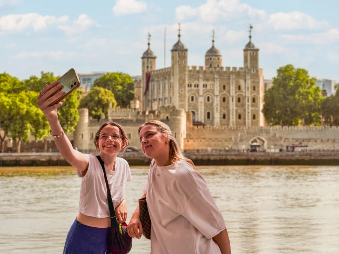 A group of tourists walking into the Tower of London with Tower Bridge in the background behind their guide from The Tour Guy.