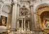 Silver processional monstrance on display inside Seville Cathedral, surrounded by detailed stone carvings and religious artwork.