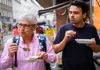 Two people eating Austrian goulash from small bowls at an outdoor food stall.