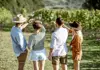 Four people standing in a vineyard holding wine glasses up to the sunlight during a tasting.