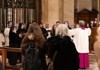 A religious ceremony takes place inside a grand basilica, with clergy members dressed in ceremonial robes leading the congregation.