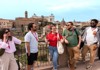 A group of travelers listens to their guide at the Roman Forum, with historic structures and columns behind them.