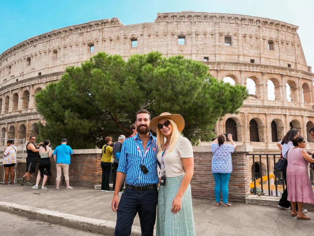A tour guide stands in front of the Colosseum, engaging with a small group of travelers while explaining its history.