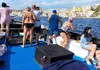 Passengers taking photos from the deck of a boat while approaching the colorful waterfront of Procida.