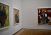 A corner of the museum displays framed paintings, with a large mirror reflecting another visitor in the room.