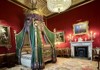 A lavishly decorated royal bedroom displays an ornate canopy bed, antique furniture, and rich red and gold decor.
