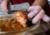 Close-up of roasted pork being sliced by a vendor wearing gloves at a street food stall.