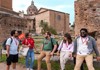 A tour guide leads a group of visitors through the ruins of the Roman Forum, with a historic domed building in the background.