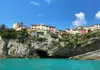 View of pastel houses built along the rocky coastline of Cinque Terre, photographed from the water.