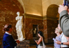 A tour guide in front of the Louis the 14th statue outside the Louvre Museum. 