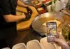 Cook preparing a flatbread wrap on a large metal griddle while a guest records with a smartphone