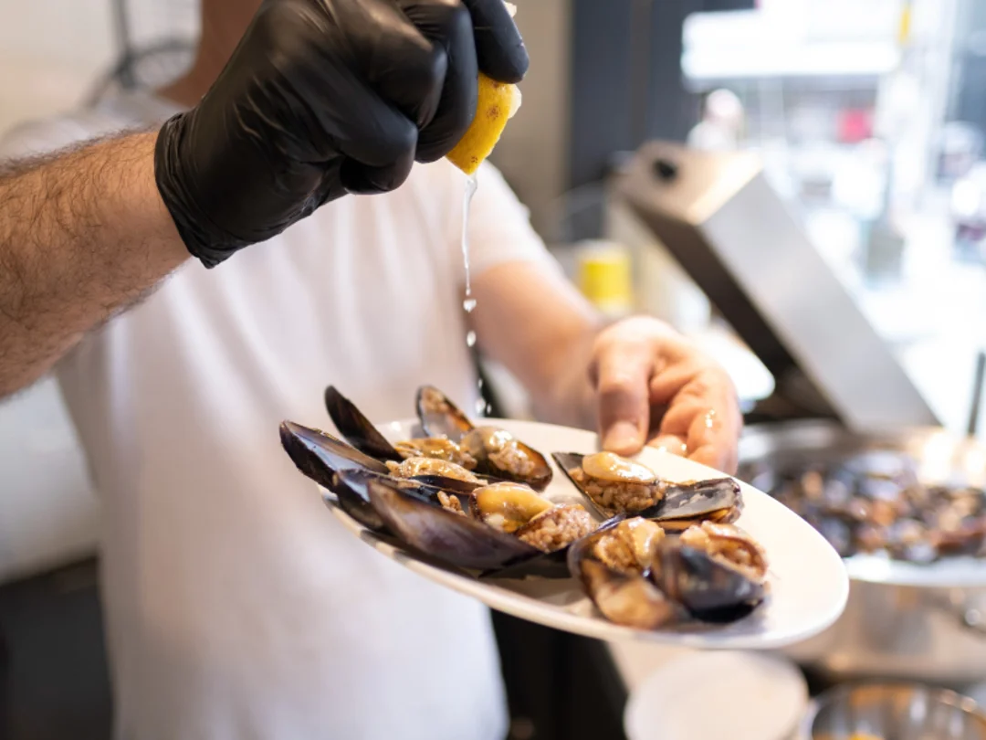 Vendor squeezing fresh lemon over a plate of steamed mussels at a seafood stall