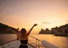 Passenger standing at the bow of a boat at sunset with Portovenere illuminated in the distance.