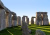 A wide-angle view of Stonehenge highlights the massive standing stones casting shadows on the bright green grass.