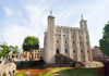A group of tourists walking into the Tower of London with Tower Bridge in the background.